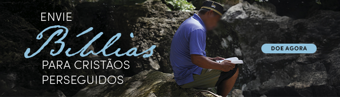 Homem do sudeste asiático sentado em pedras com uma Bíblia nas mãos