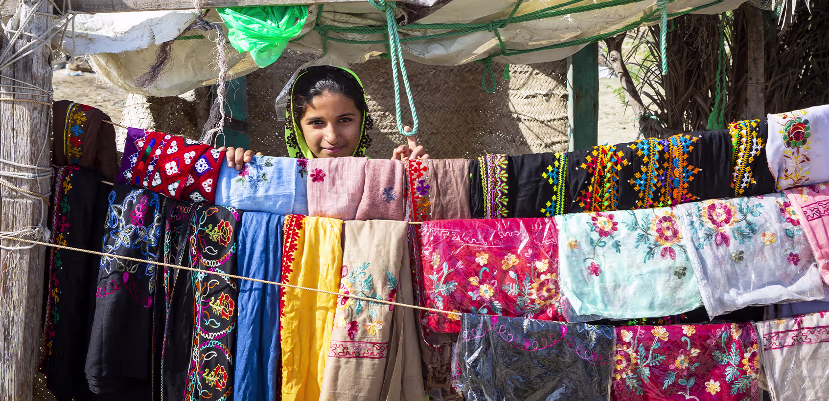 Menina iraniana atrás de um varal com tecidos coloridos