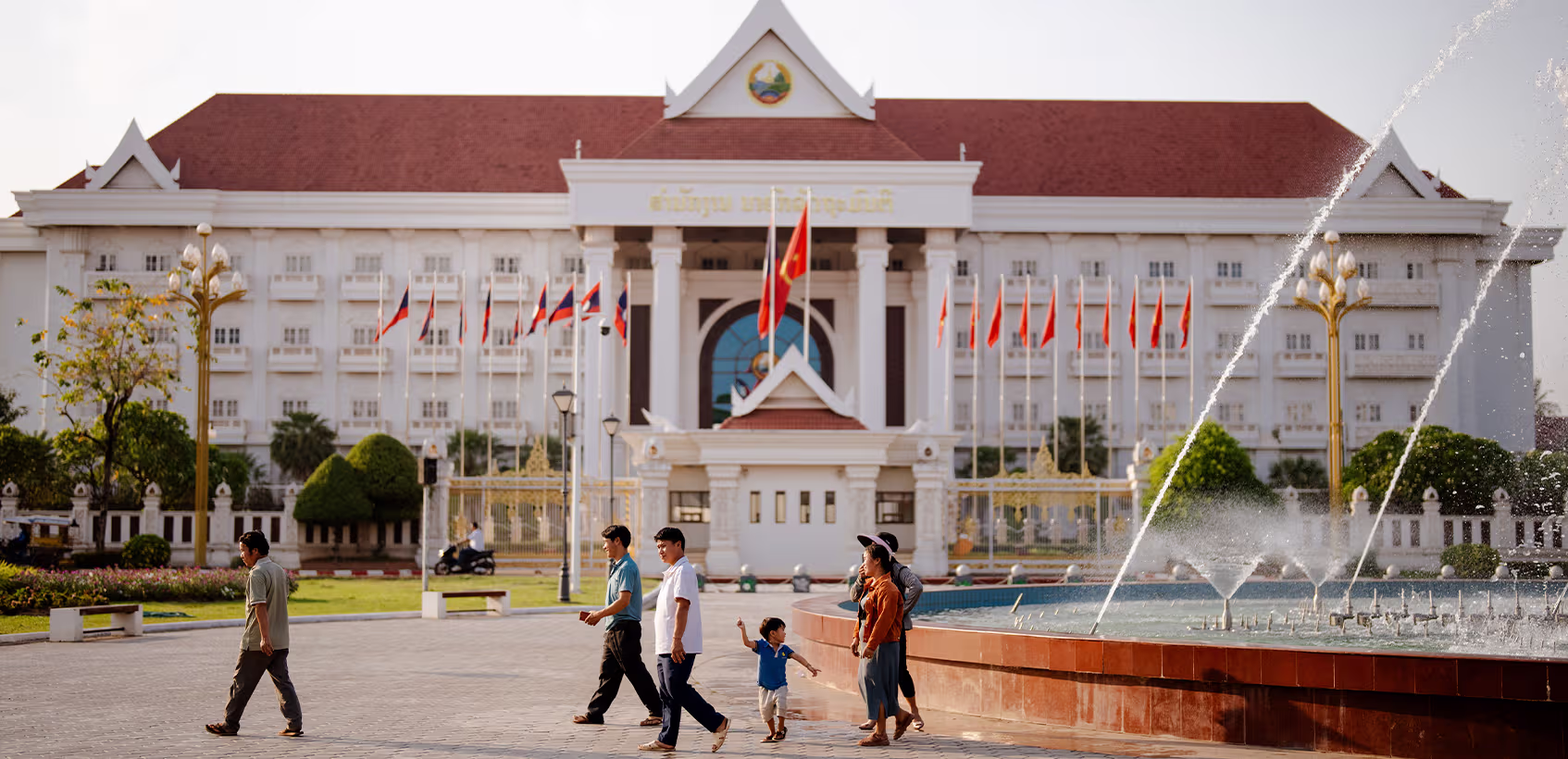 Família no Laos caminha em frente a uma fonte